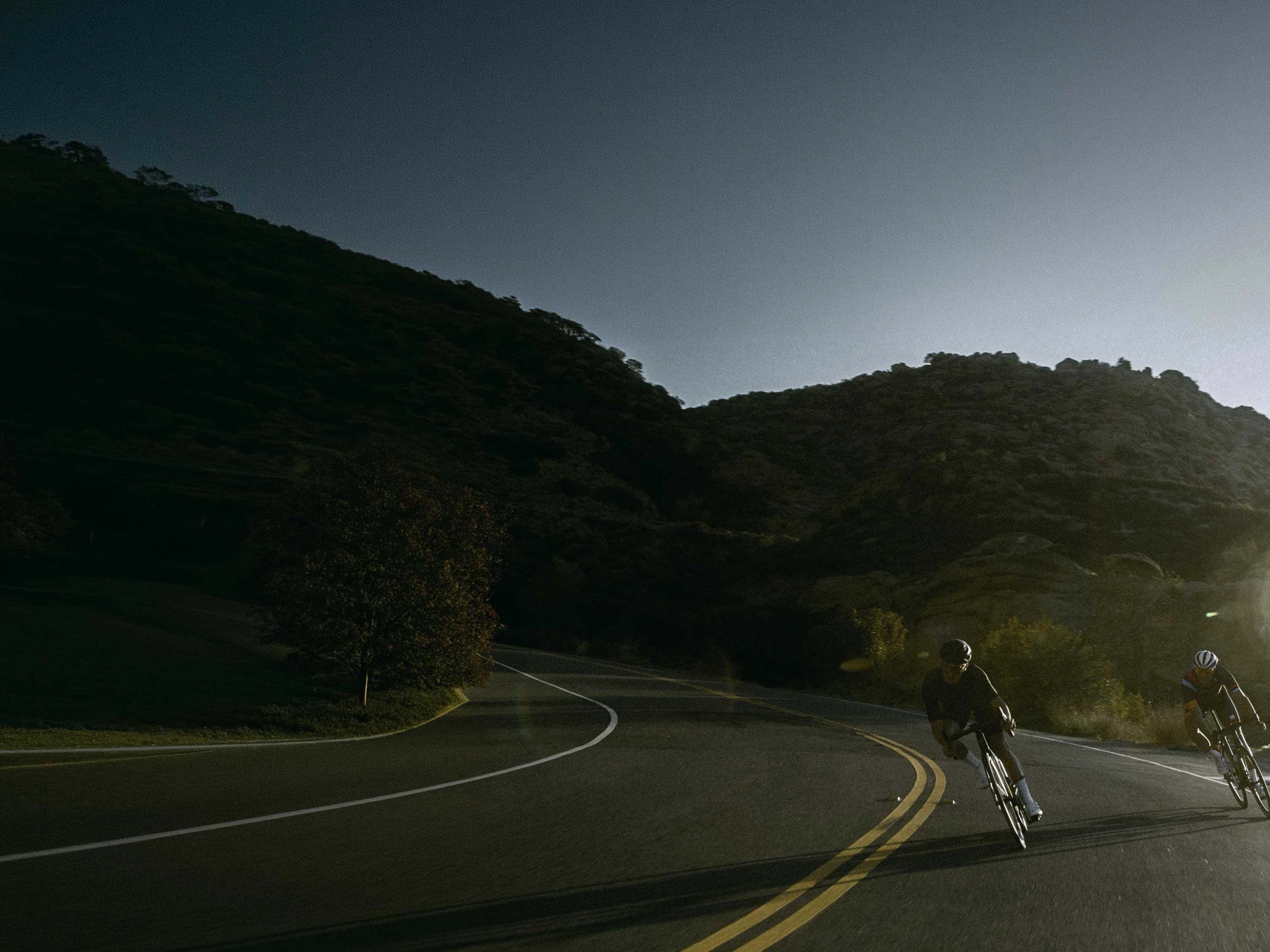 Two cyclists riding on a winding mountain road at golden hour