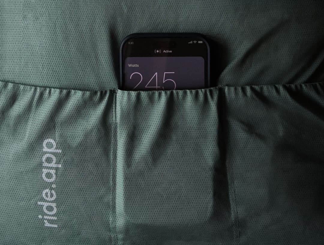 iPhone tucked into a cycling jersey pocket showing live wattage
